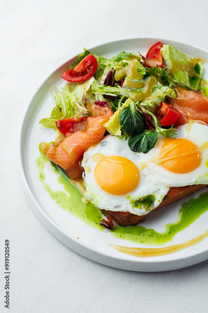 Breakfast, two eggs served on toasted bread with a green herb sauce. Accompanied fresh salad, cherry tomatoes, and smoked salmon slices, all elegantly presented on a white plate and white background Breakfast, two eggs served on toasted bread with a green herb sauce. Accompanied fresh salad, cherry tomatoes, and smoked salmon slices, all elegantly presented on a white plate and white background