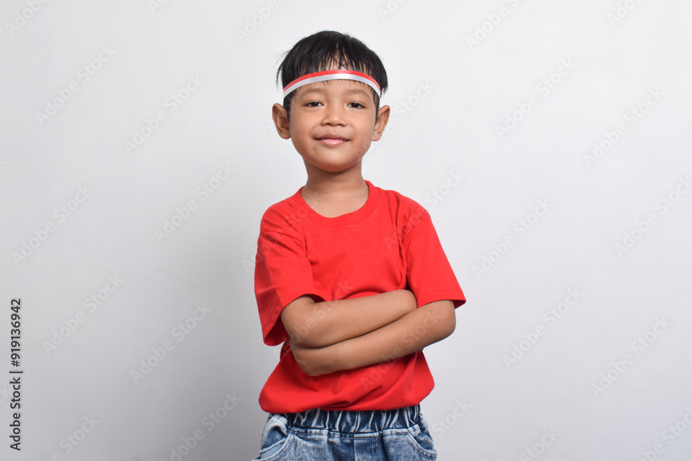 A cheerful Indonesian boy in a red shirt stands with his arms crossed, isolated on a white background. Indonesian Independence Day concept. A cheerful Indonesian boy in a red shirt stands with his arms crossed, isolated on a white background. Indonesian Independence Day concept.