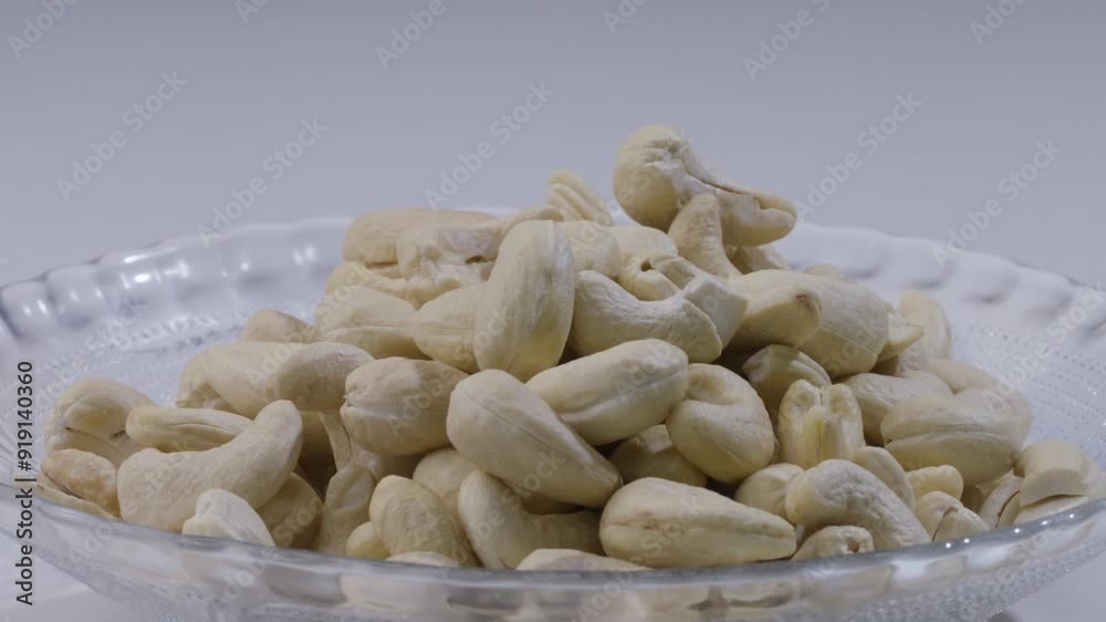 Close up of hand picking up handful of cashew nuts from plate on table. Static Close up of hand picking up handful of cashew nuts from plate on table. Static