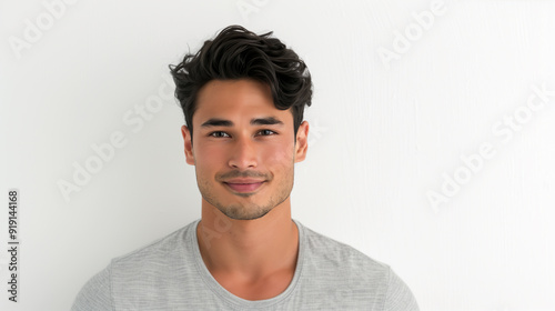 Close-up of a smiling young trans masculine Asian man with neatly styled hair, wearing a light gray shirt, set against a plain white background, radiating warmth and confidence.