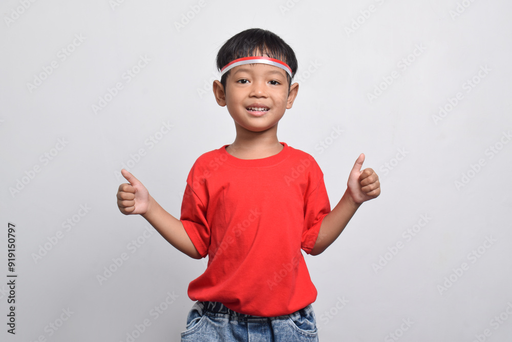 A happy Indonesian boy in red shirt giving thumbs up, isolated on white background. Indonesian Independence Day concept. A happy Indonesian boy in red shirt giving thumbs up, isolated on white background. Indonesian Independence Day concept.
