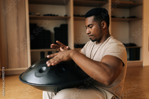 Focused African man in trance enjoying playing by hands on glucophone sitting cross-legged on floor at home. Silence calm filling room by sounds of music from musical instrument. photo