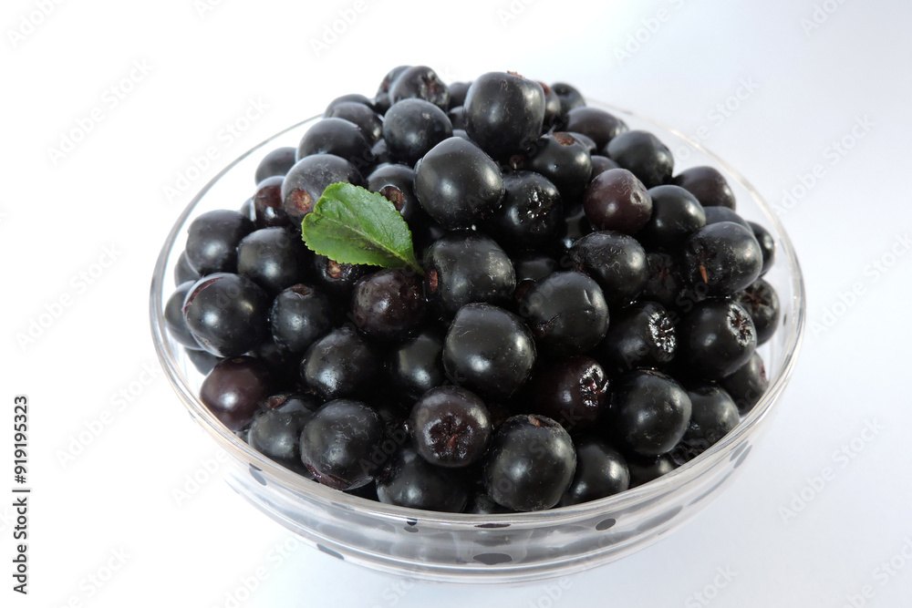 Fresh aronia berries decorated with a green leaf in a glass bowl, white background Fresh aronia berries decorated with a green leaf in a glass bowl, white background