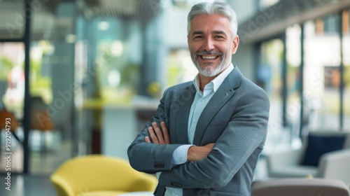 Smiling handsome businessman with crossed arms in modern office, middle-aged gray-haired man exuding confidence, business success concept.