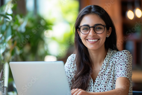 Happy latin hispanic young business woman working on laptop computer in company office. Smiling Indian entrepreneur manager businesswoman using pc for communication, learning at workplace