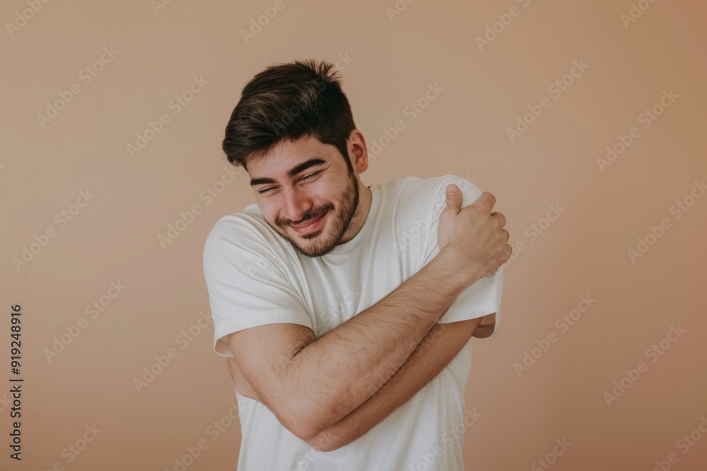 Young man hugging himself on a beige background, happy concept of self love Young man hugging himself on a beige background, happy concept of self love