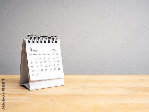 The white September 2024 desk calendar for plan and reminder isolated on wooden table and grey background with copy space. Small minimal calendar with page of 9th month, business schedule concept.