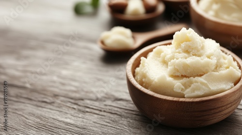 Photograph featuring a wooden bowl filled with creamy, natural shea butter placed on a rustic wooden tabletop, emphasizing the texture and purity of the shea butter.