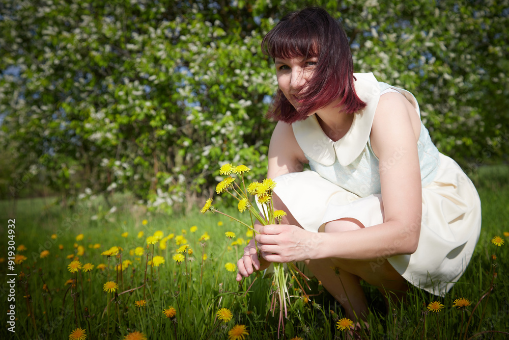 Portrait of beautiful young woman near apple trees and yellow dandelion flower in park on a sunny day. Springtime Portrait of beautiful young woman near apple trees and yellow dandelion flower in park on a sunny day. Springtime