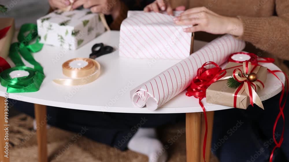close-up white table with red and gold ribbon various wrapping paper rolls and presents. concept: unrecognizable no face packaging gift for winter holidays christmas 