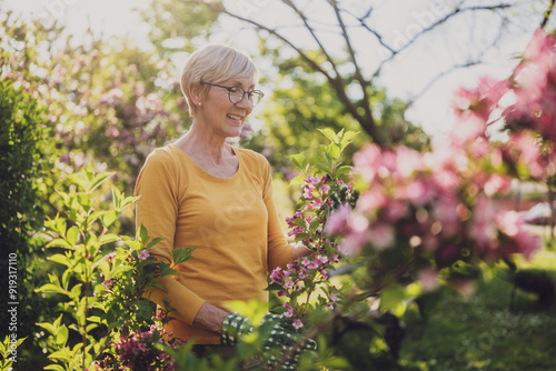 Happy senior woman enjoys looking at flowers in her garden.	