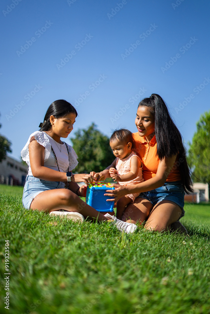 Young Latin family in a park. Family of a young mother, a teenage aunt and a baby girl playing together in a park on a sunny day Young Latin family in a park. Family of a young mother, a teenage aunt and a baby girl playing together in a park on a sunny day