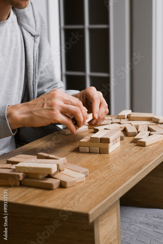 person stacks wooden blocks to construct tower on table in a room, Man playing table game for concentration at home. Digital detox