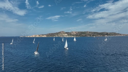 Aerial drone footage of sailboats racing near Sardinia coast on sunny day. Perfect shot for travel, tourism, luxury, and sailing lifestyle.