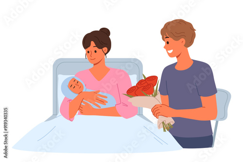 Woman given birth lies in hospital bed, showing baby to happy father with flowers. Girl who has given birth and happy man rejoicing at nascency of son or daughter after long pregnancy