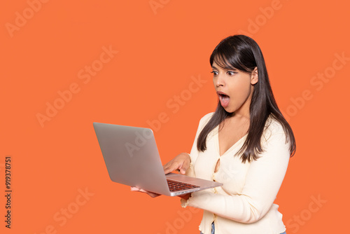 Woman With Long Hair Expresses Surprise While Using Laptop Against Orange Background