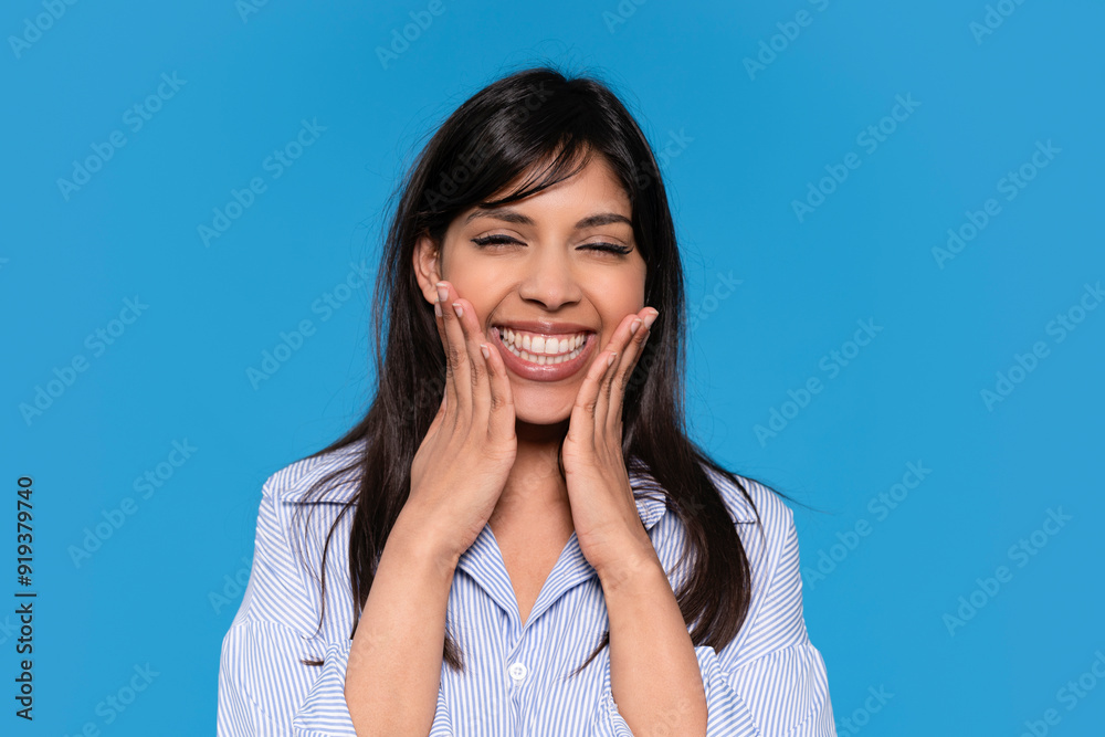 Woman Smiling With Hands on Her Cheeks Against Bright Blue Background Woman Smiling With Hands on Her Cheeks Against Bright Blue Background