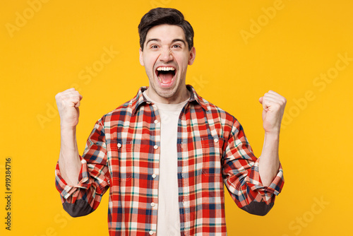 Young cool cheerful happy man he wears red checkered shirt casual clothes doing winner gesture celebrate clenching fists isolated on plain yellow orange background studio portrait. Lifestyle concept.