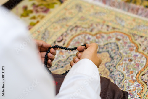 Close up Rear view shot of a hand man holding prayer beads, set against a colorful, patterned carpet. The photo captures a moment of reflection and spirituality. Ideal for content related to religion. photo