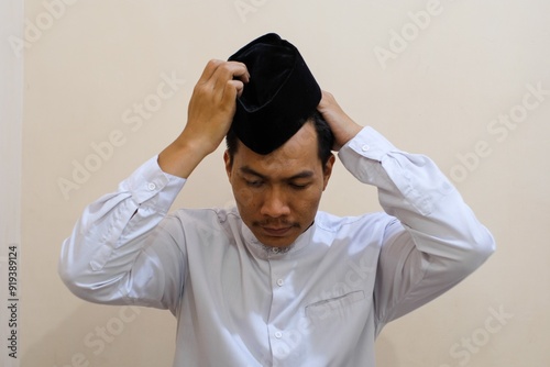 Portrait of A Southeast Asian man wearing white shirt putting Muslim prayer cap called Peci on his head, called peci or songkok. photo