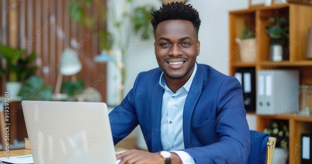 Happy African American businessman in blue suit, sitting at desk with laptop, looking away, working. Happy African American businessman in blue suit, sitting at desk with laptop, looking away, working.
