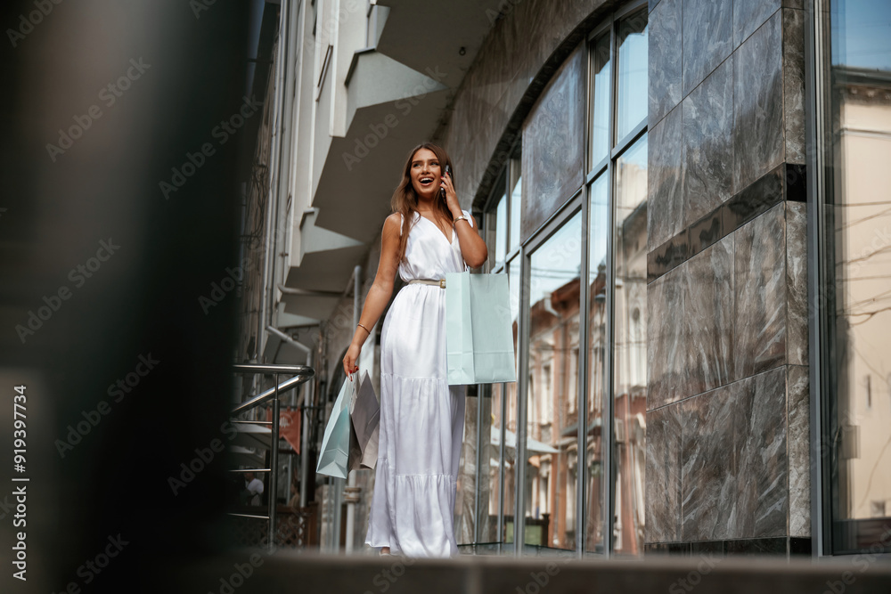 Talking by a phone. Stylish woman is with shopping bag outdoors near the building Talking by a phone. Stylish woman is with shopping bag outdoors near the building