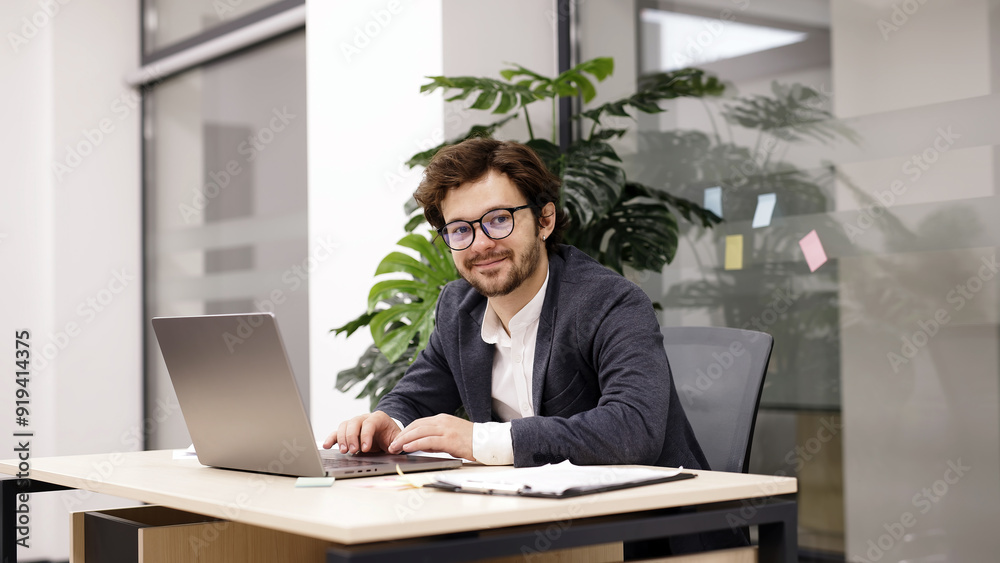 A charismatic young programmer sits confidently in a modern office, looking at the camera beside his laptop. Perfect for themes of tech professionals, modern workspaces, and career confidence. A charismatic young programmer sits confidently in a modern office, looking at the camera beside his laptop. Perfect for themes of tech professionals, modern workspaces, and career confidence.