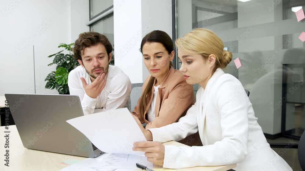 Business team in a modern office using a laptop for financial analysis. They brainstorm and discuss a corporate project, collaborating on solutions. Perfect for teamwork and financial strategy themes.