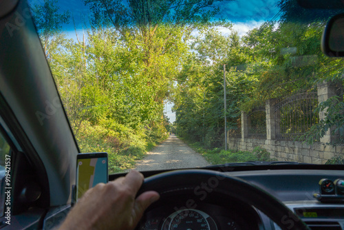 View from the windshield of a car onto a shady dirt road between green trees