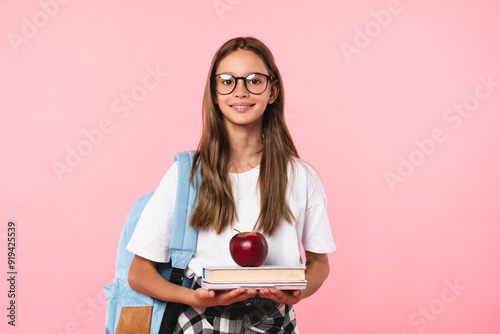 Best student pupil teenage girl with excellent marks going back to school with books and apple isolated in pink background. New academic educational year begins starts.