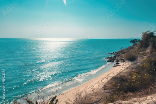 Sunny day at a serene beach with light blue ocean and clear horizon line. Lush green foliage on the shore. Great for photography or simply enjoying the natural beauty.