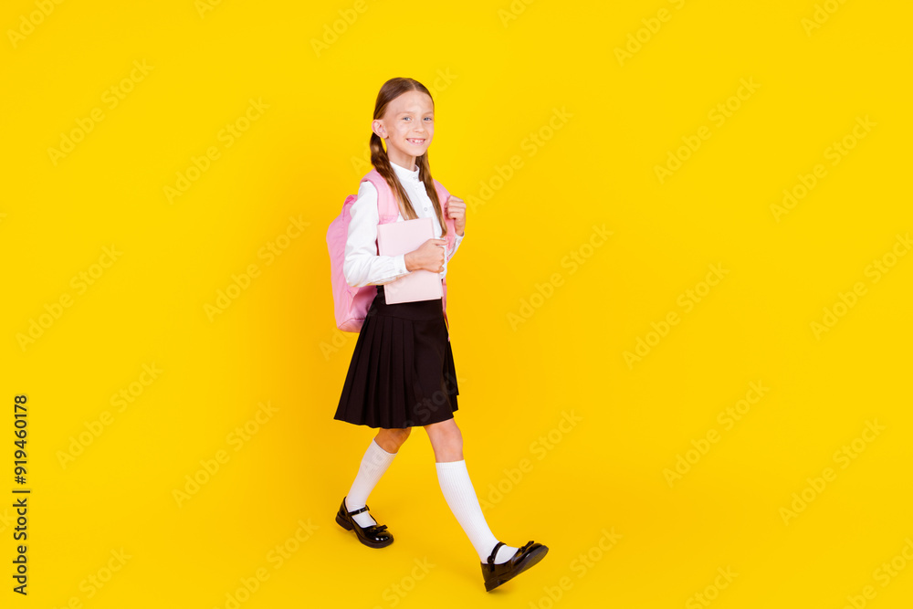 Full body photo of cute little schoolgirl diligent backpack walking dressed stylish uniform isolated on yellow color background Full body photo of cute little schoolgirl diligent backpack walking dressed stylish uniform isolated on yellow color background
