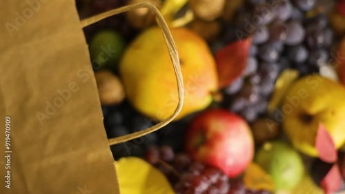 Autumn harvest of apples, pears, walnuts, prunes, and grapes spills from a paper bag onto a table, accompanied by vibrant fall leaves. Natural and eco-friendly packaging 