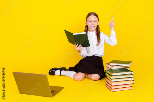 Full body photo of little schoolgirl diligent online lesson read book eureka dressed stylish uniform isolated on yellow color background