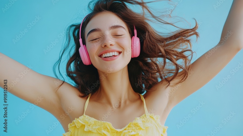 Elegant and carefree scene of a young woman with dark brown hair and pink headphones dancing in a yellow halter top and flowy skirt against a light blue background. Happiness and lifestyle concept Elegant and carefree scene of a young woman with dark brown hair and pink headphones dancing in a yellow halter top and flowy skirt against a light blue background. Happiness and lifestyle concept