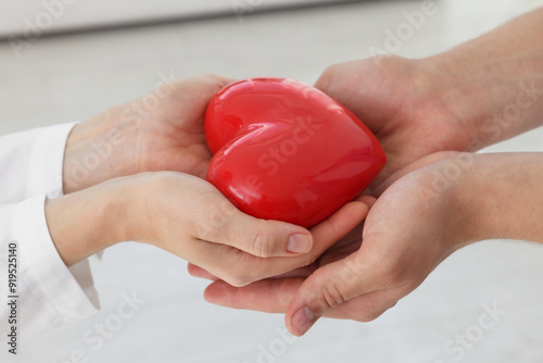 Doctor giving red heart to patient at white table in clinic, closeup