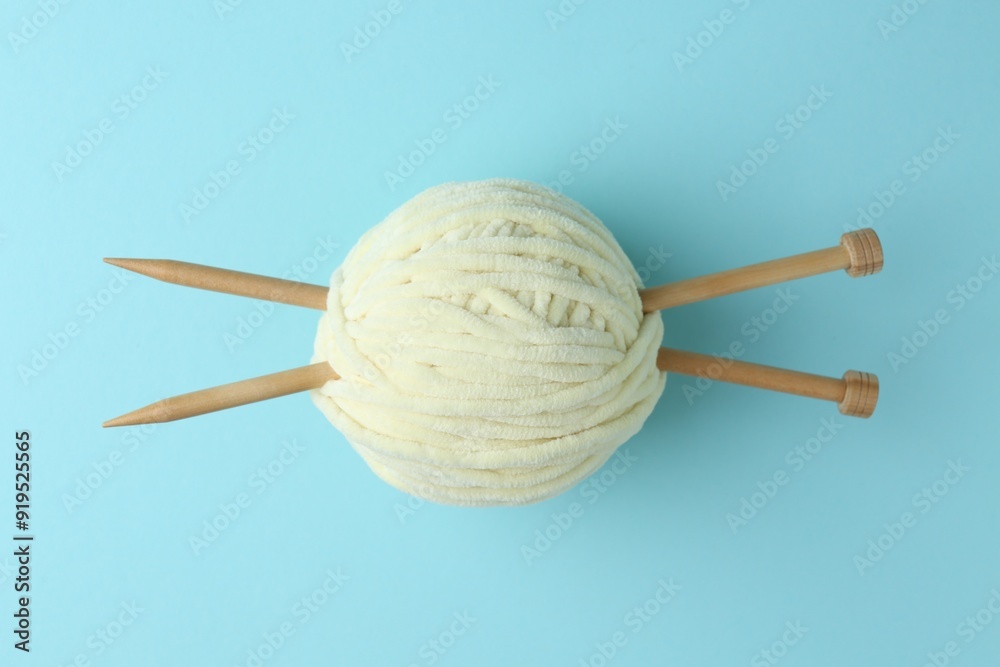 Ball of plush yarn with knitting needles on light blue background, top view Ball of plush yarn with knitting needles on light blue background, top view