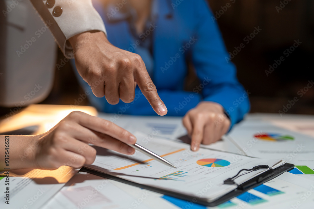 Two people are looking at a table with a lot of graphs and charts Two people are looking at a table with a lot of graphs and charts