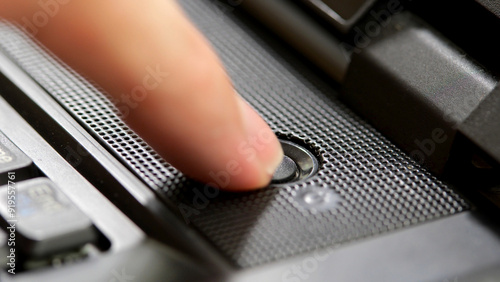 Tableau sur toile Finger pressing a generic round dark black power button on a simple office laptop, closeup detail, one person