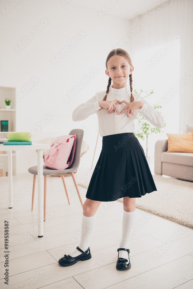 Vertical photo of cute small schoolkid show heart wear uniform living room apartment indoors Vertical photo of cute small schoolkid show heart wear uniform living room apartment indoors