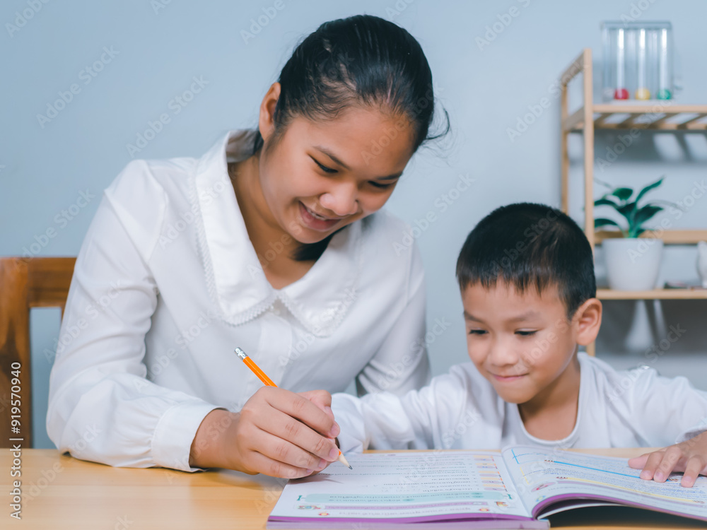 Teacher or mother helping boy writing lesson and learning to write, Female tutor helping little elementary school boy with homework during individual lesson at home, Education home school concept. Teacher or mother helping boy writing lesson and learning to write, Female tutor helping little elementary school boy with homework during individual lesson at home, Education home school concept.