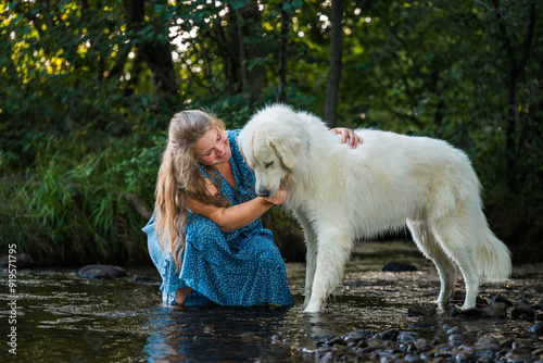 Young woman and her large white Great Pyrenees dog enjoying time together, cooling off in a stream during hot summer day. Pet owner, pet love, dog frienship concept. photo