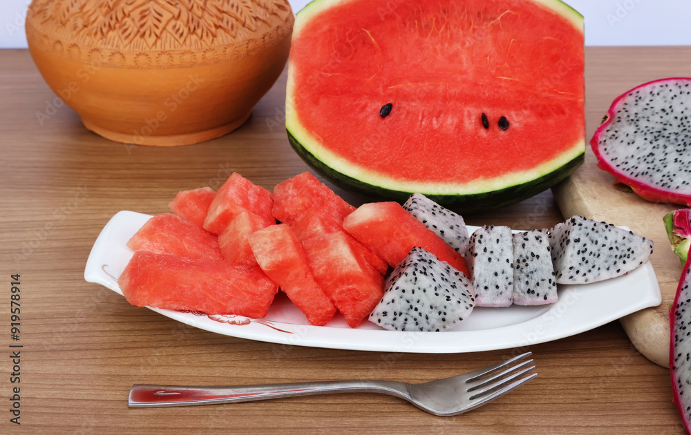 Watermelon and dragon fruit cut in a white porcelain plate and cut in half placed on the back on a wooden table with a white background.
Watermelon and dragon fruit cut in a white porcelain plate and cut in half placed on the back on a wooden table with a white background.