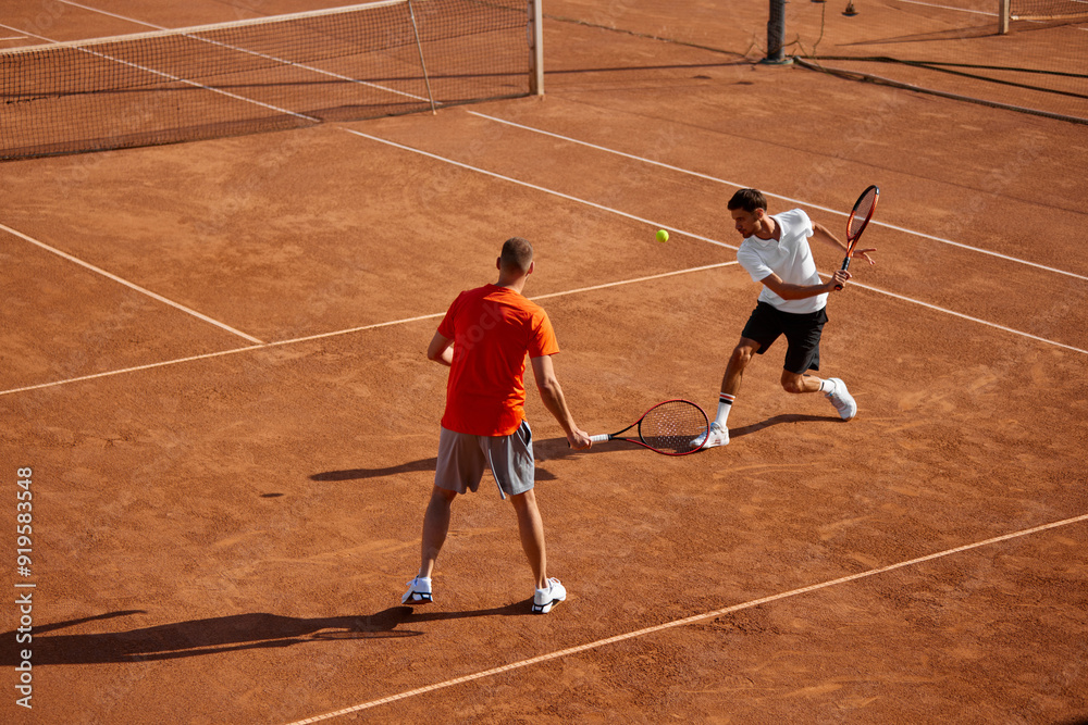 Two men, tennis players in motion on outdoor clay court, showing game skills and teamwork cooperation, playing with focus. Concept of sport, competition, active and healthy lifestyle Two men, tennis players in motion on outdoor clay court, showing game skills and teamwork cooperation, playing with focus. Concept of sport, competition, active and healthy lifestyle