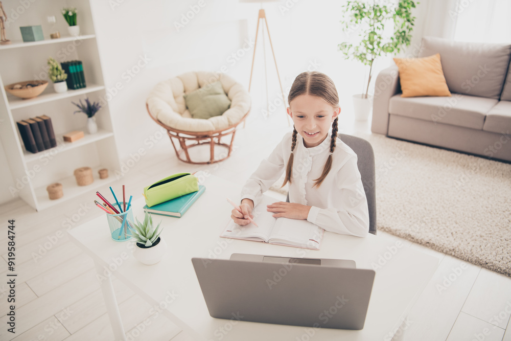Photo of cute small girl study online laptop desk write notepad modern apartment indoors Photo of cute small girl study online laptop desk write notepad modern apartment indoors