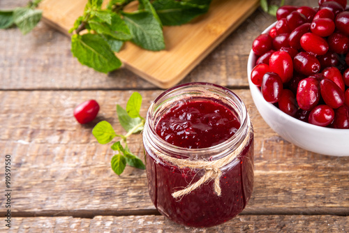 Cornelian cherry, dogwoods edible berry jam or marmalade in small jar with fresh berries on kitchen table, copy space