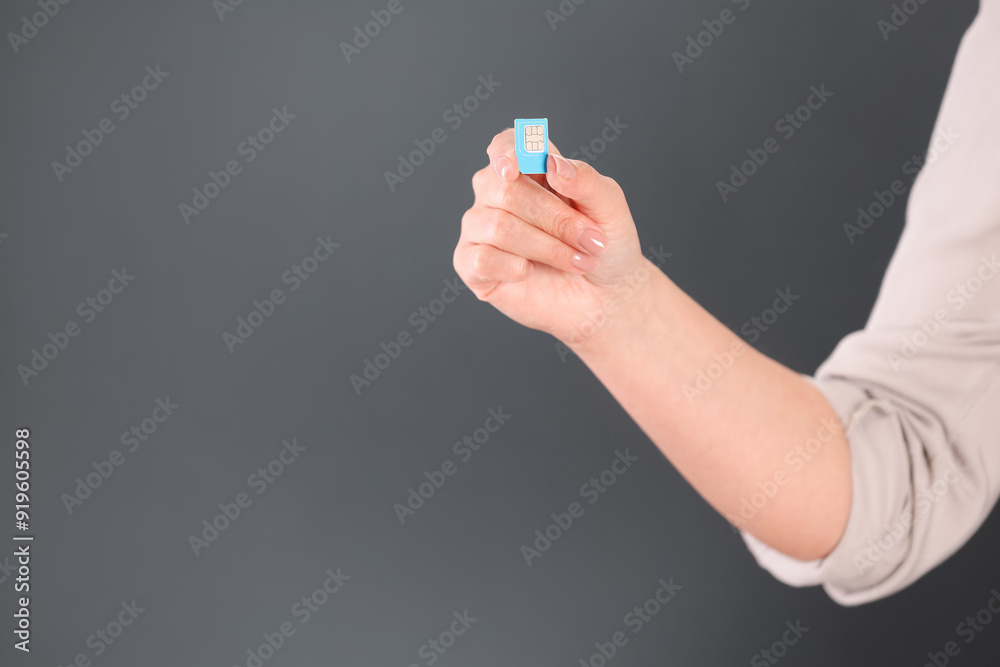 Woman holding SIM card on dark grey background, closeup. Space for text Woman holding SIM card on dark grey background, closeup. Space for text