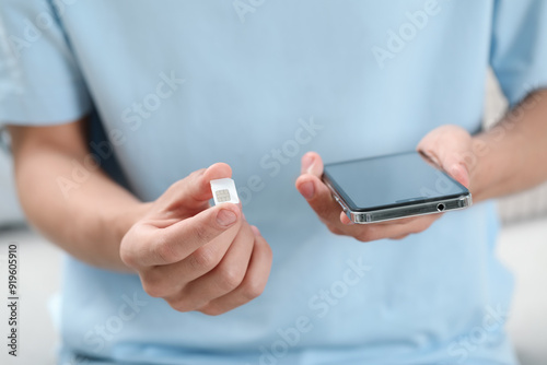 Man with SIM card and smartphone indoors, closeup photo