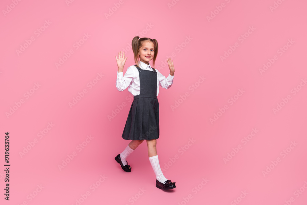 Full size photo of charming little pupil girl walking wave hand hi wear trendy uniform isolated on pink color background Full size photo of charming little pupil girl walking wave hand hi wear trendy uniform isolated on pink color background