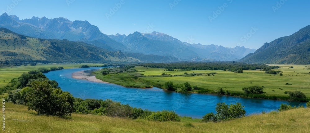 Obraz premium A river runs through a verdant valley, surrounded by lush green grass and mountains The valley is blanketed with greenery
